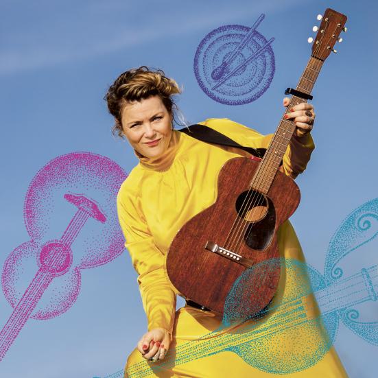 Stine Michel i en gul kjole med en guitar i hånden