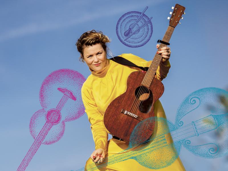 Stine Michel i en gul kjole med en guitar i hånden