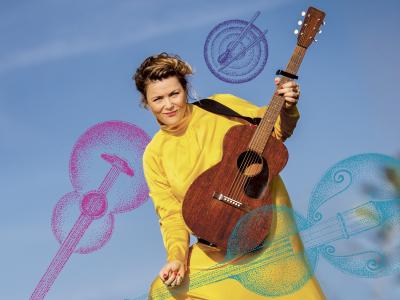 Stine Michel i en gul kjole med en guitar i hånden